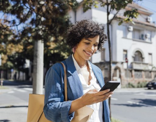 A mixed-race businesswoman reading something funny on her mobile phone on the street while going back home from work.